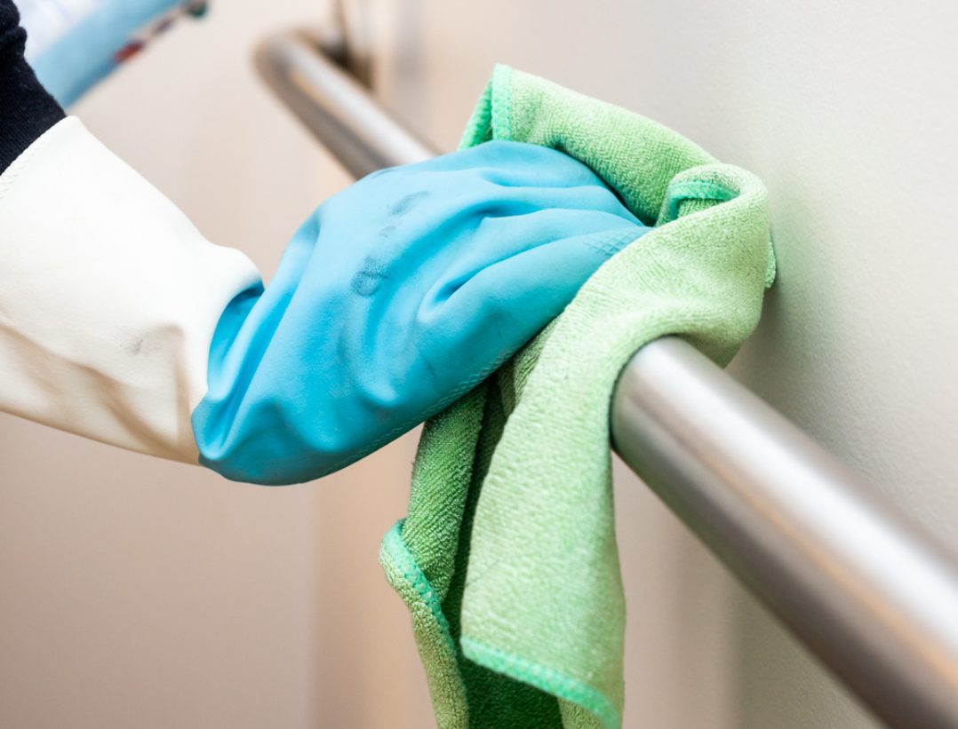 A person providing disinfecting services to a handrail with disinfecting solution and a cloth.
