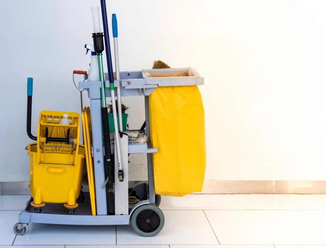 A yellow cleaning cart with buckets and mop.